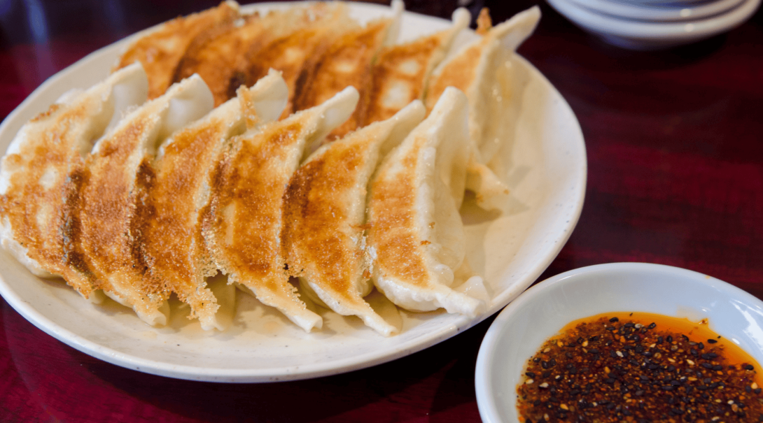 Japanese fried gyoza on a white plate with a chilli dipping sauce